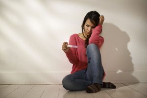 Woman looking at pregnancy test kit, sitting on ground at home